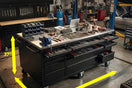 Large black tool workbench with drawers, wheels, organized tools, and size measurements in workshop