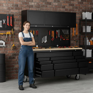 Woman in overalls standing by a tool workbench with black storage drawers in a workshop.