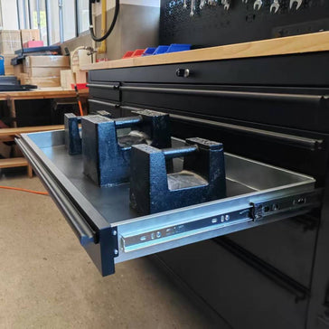 Heavy-duty tool chest drawer open with metal weights testing drawer slides in workshop
