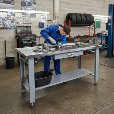 Mechanic working at metal workbench in garage workshop with tool storage and tires