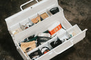 White toolbox filled with various items on a dark surface.