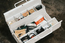 White toolbox filled with various items on a dark surface.
