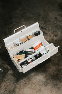 White toolbox filled with various items on a dark surface.