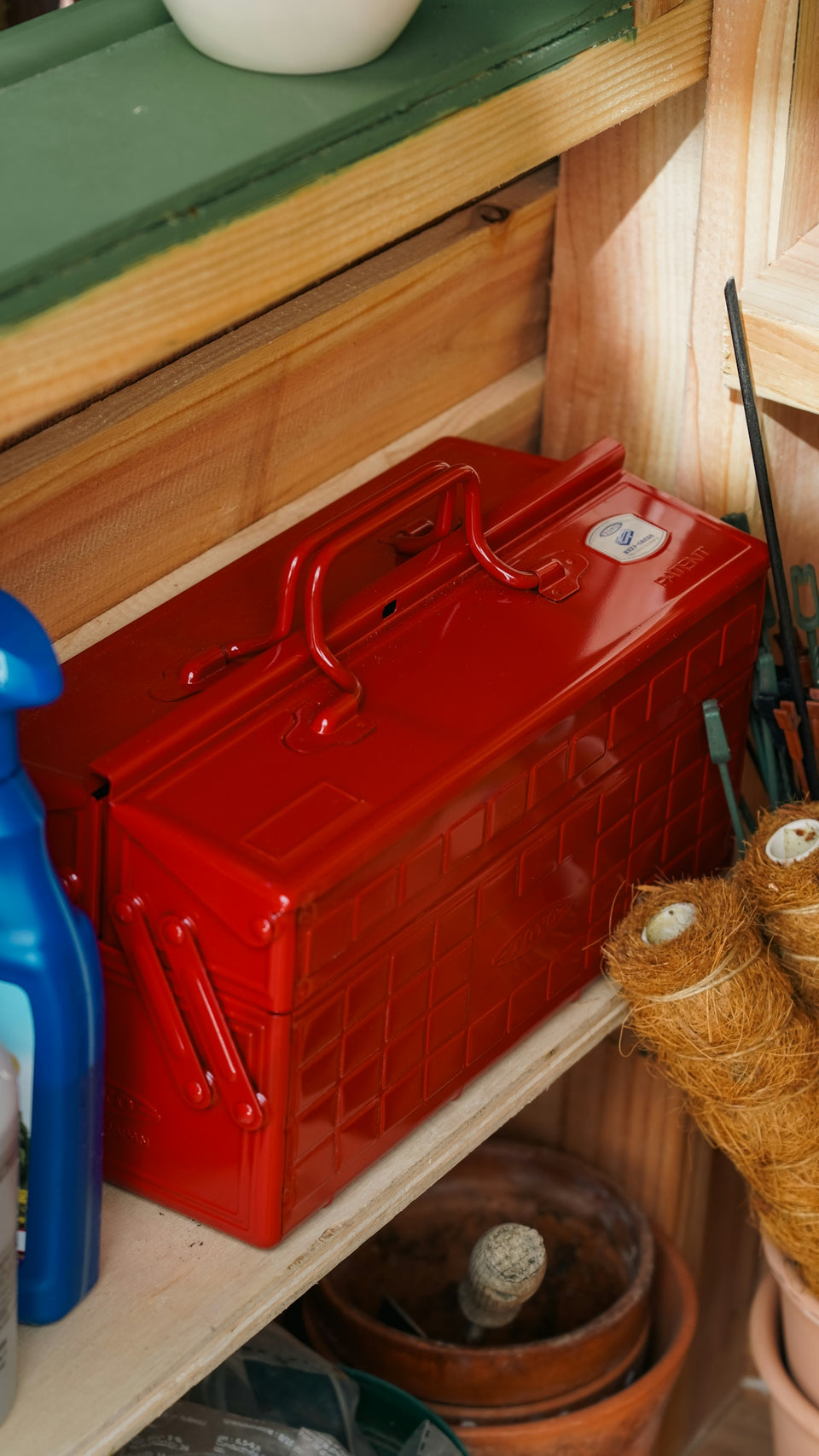 A red toolbox sits on a shelf with gardening supplies.
