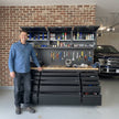 Man standing in a garage next to a large tool chest with tools and equipment on shelves.